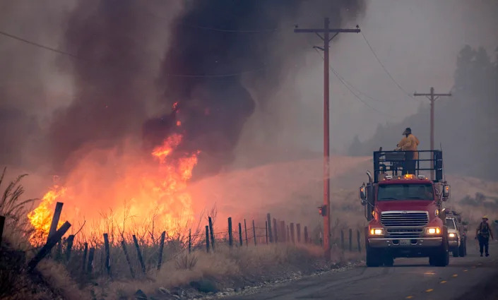 A makeshift fire truck shoots water on a wildfire from the road.